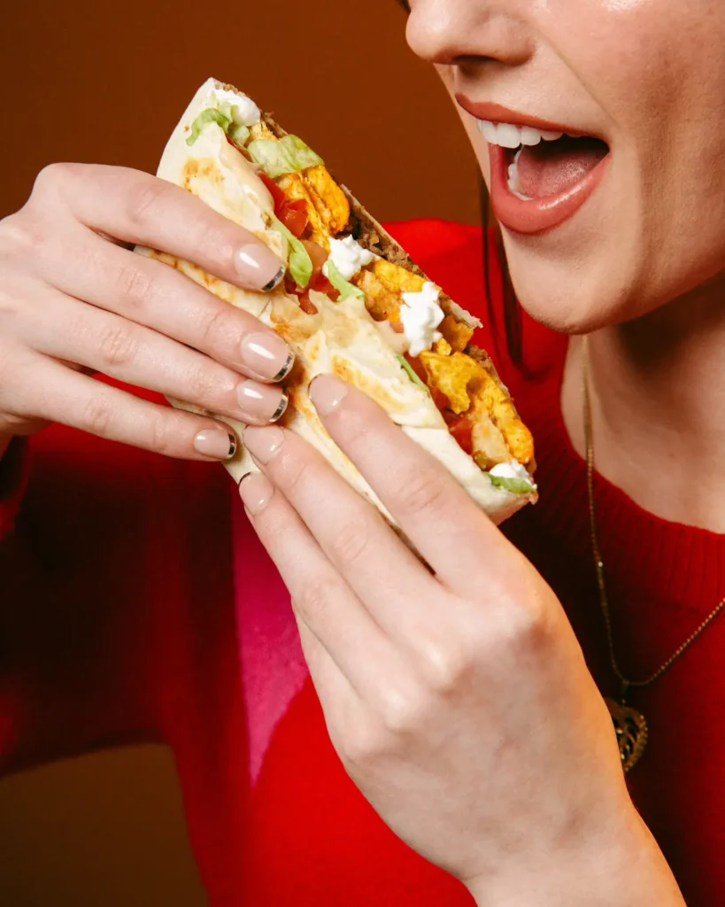 Close-up of a person biting into a taco filled with seasoned chicken, lettuce, tomatoes, and sour cream.