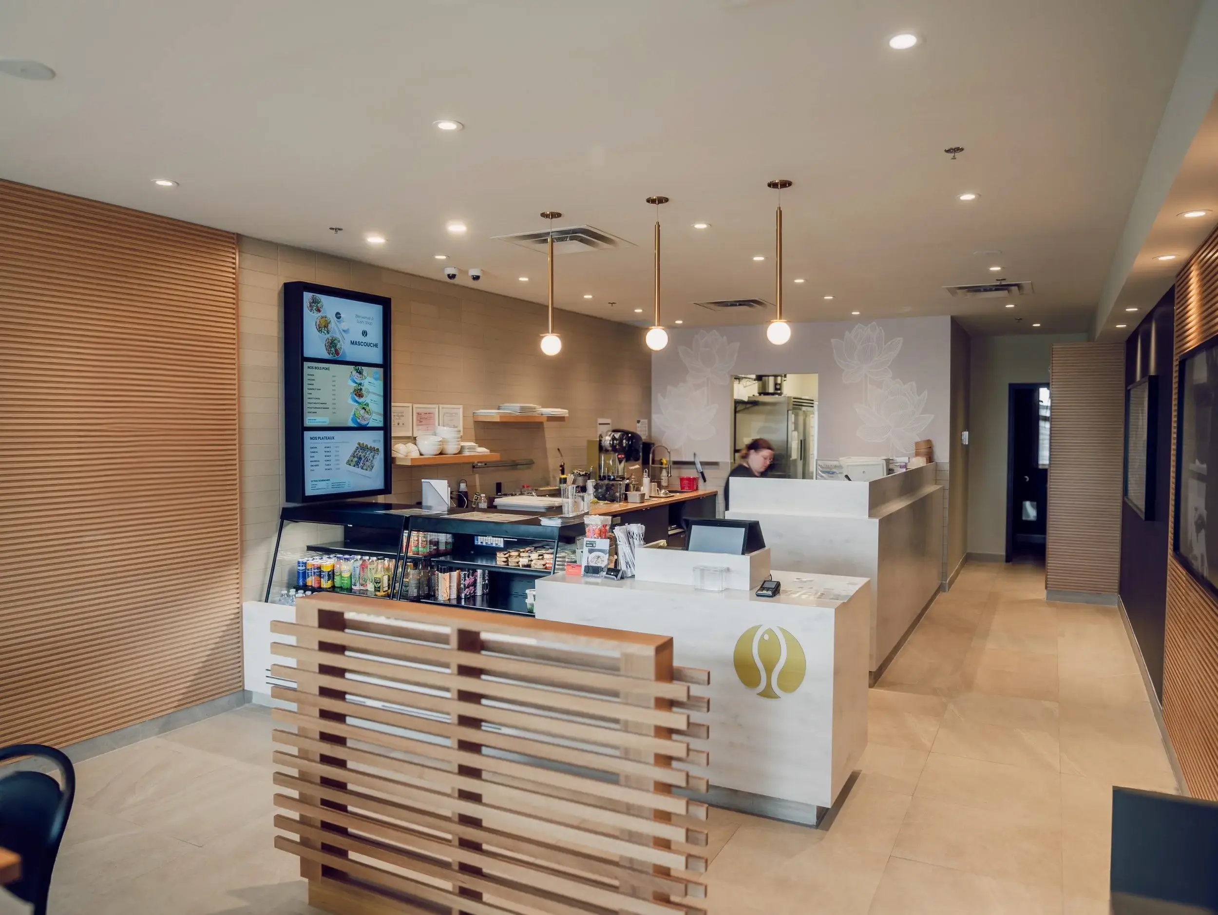 Interior of a Sushi Shop location showing the front counter, digital menu boards, refrigerated display case and warm wood slat walls.