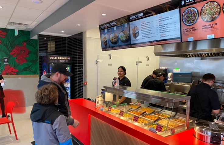 Manchu WOK team members serving guests at a red counter inside a street location.