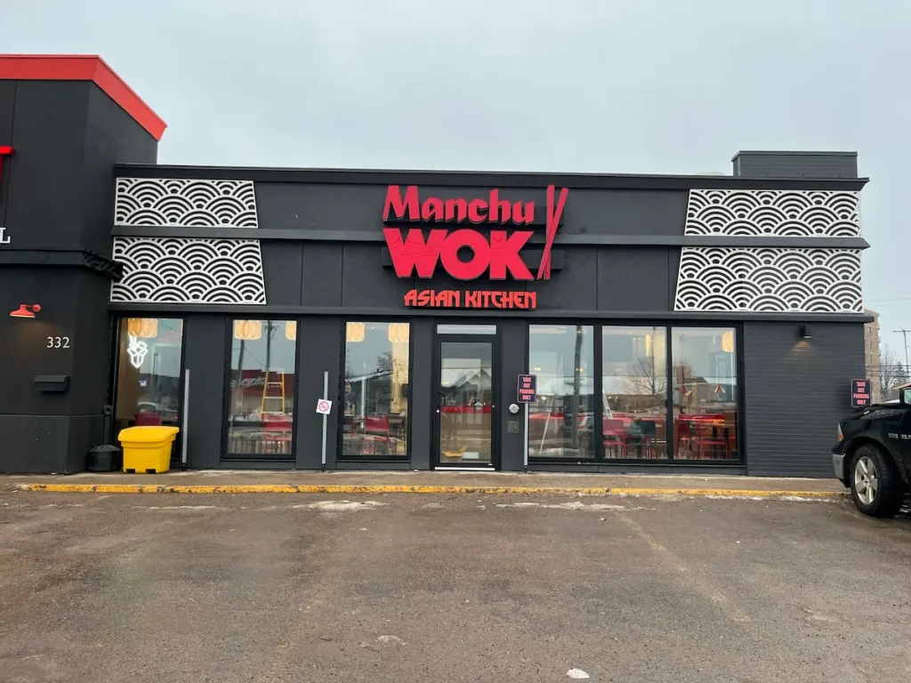 Exterior of a freestanding Manchu WOK Asian Kitchen street location with red signage.